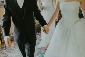 Home A romantic moment capturing a bride and groom holding hands in elegant wedding attire indoors.